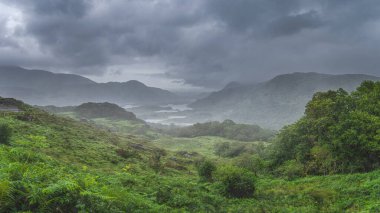 Atmosferik, dramatik fırtına gökyüzü ve bulutlar, İrlanda ikonik bakış açısıyla sisli ve şiddetli yağmur, Bayanlar Görünümü. Göllü yeşil vadi. Kerry Pisti, İrlanda