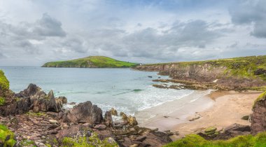 Dingle Deniz Feneri, dönen balıkçı teknelerine rehberlik ediyor. İnsanlar Atlantik Okyanusu 'nun soğuk sularında yüzüyor. Uçurumlar arasında gizli sahil, Kerry, İrlanda