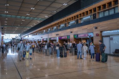 Berlin, Almanya 8 Ağustos 2021 işlek bir Brandenburg Havaalanı terminalinde, çok sayıda gezgin bavullarıyla hareket halindeki alanda, dijital bilgi içeren kontrol tezgahlarının yanında geziniyor.