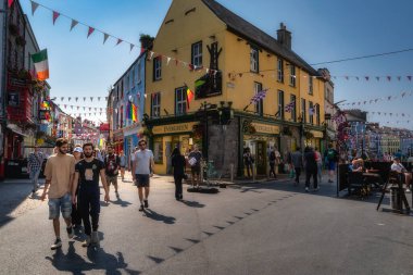 Galway, İrlanda, 26 Ağustos 2021 Sunlit renkli cadde turistlerle dolu canlı meydanda barlar, kafeler, festival kiraz çiçekleri, açık hava koltukları. Sıcak yaz aylarında gezen çiftler ve gruplar