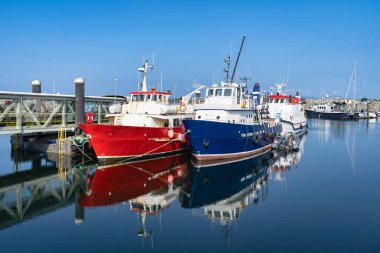 Renkli balıkçı tekneleri ve Galway, Rossaveel, İrlanda 'nın sakin yüzeyinde parlak yansımaları olan huzurlu bir rıhtım. Idyllic limanı berrak gökyüzünün altında demirli balıkçı tekneleri sergiliyor