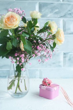 Masanın üzerinde bir vazo çiçek olan pembe hediye kutusu.