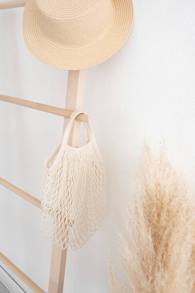 knitted cotton string bag and beach hat on stairs against white wall backgroun