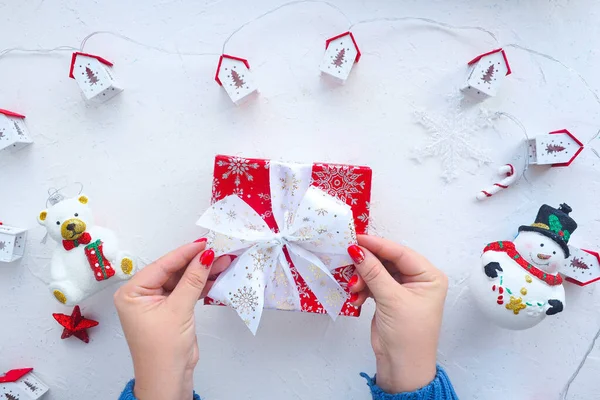 女性の手が可愛いクリスマスツリーのおもちゃと家の庭と白いテーブルの上にクリスマスプレゼントを包んでいます — ストック写真