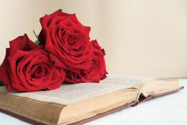 three red roses on an open old book on a table on a beige background