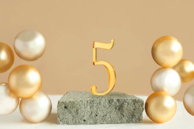 Beton bir podyumda 5 numara ve bej arka planda hacimli altın toplar. Boşluğu kopyala