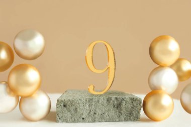 Beton bir podyumda 9 numara ve bej arka planda hacimli altın toplar. Boşluğu kopyala