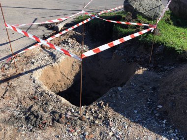 Çukur tadilat sırasında kırmızı ve beyaz şeritlerle çevrilmiş. Yoldaki toprak işleri.