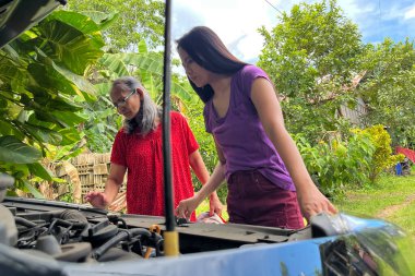 Kadınlar motor arızası bulmak için bozuk bir arabanın altına bakar..