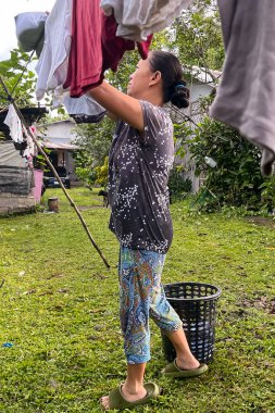 Asyalı bir kadın çamaşırlarını bahçeye asıyor..