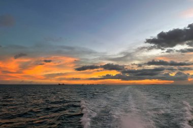 Canlı turuncu ve sarı gökyüzü ile huzurlu okyanus gün batımı, tekne uyanıyor.