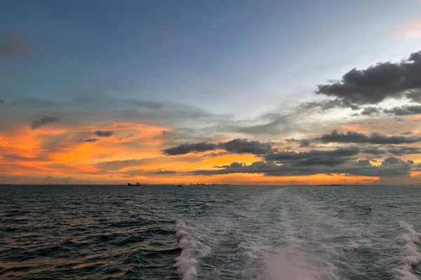 Canlı turuncu ve sarı gökyüzü ile huzurlu okyanus gün batımı, tekne uyanıyor.