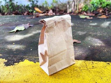 Güz yapraklı sarı ve gri bir yüzey üzerinde kahverengi kağıt torba, öğle yemeği veya bakkaliye için basit çevre dostu paket, yan görüş, doğal ve tek kullanımlık.