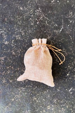 Yeniden kullanılabilen küçük doğal çevre dostu kahverengi bej renkli çuval çantası. Arkaplanı koyu dokulu hediye ya da depolama için kullanılabilir..