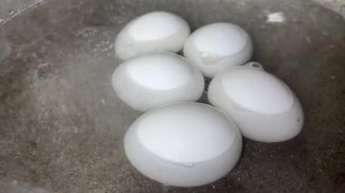 Metal tencerede kaynayan suda kaynamış beyaz tavuk yumurtalarının yakın çekimi.