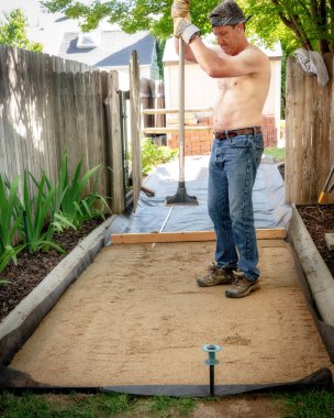 Bahçe düzenleyicisi bir patika üzerindeki kumu düzleştirmek için çalışır