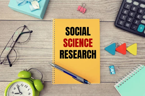 Social Science Research is written on a notepad, on an office desk with office accessories.