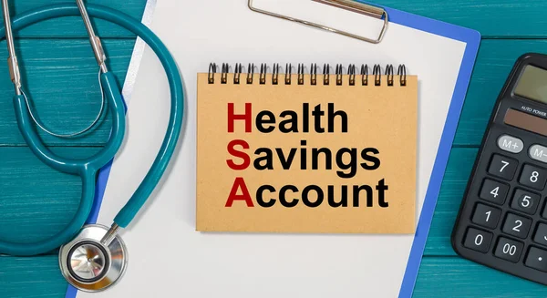 Notepad with text Health Savings Account HSA, calculator and stethoscope. Medical concept.