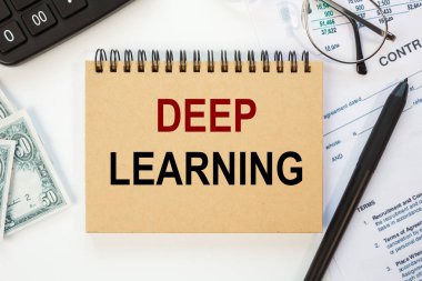 Ofis masasının üzerindeki defterde ofis malzemeleriyle birlikte derin öğrenme yazılıdır..