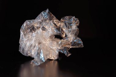 Siyah arka planda buruşmuş bir polietilen parçası. İnorganik atık. Ekoloji ve atık geri dönüşüm kavramı.