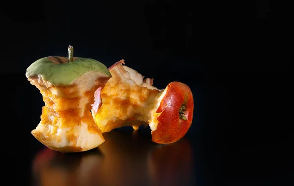 An apple core on a black background with reflexion. Ecology and garbage recycling concept.