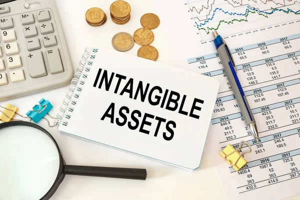 Intangible assets is written on a notepad on an office desk with office accessories.