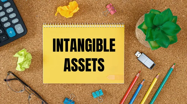Intangible assets is written on a notepad on an office desk with office accessories.