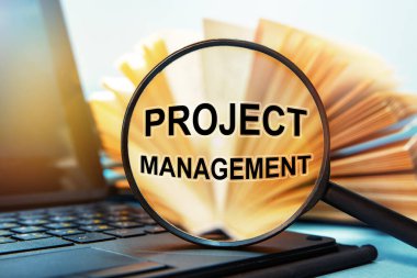 Dizüstü bilgisayar ve büyüteçle kitap. Büyüteçle ilgili metin projemiz var..