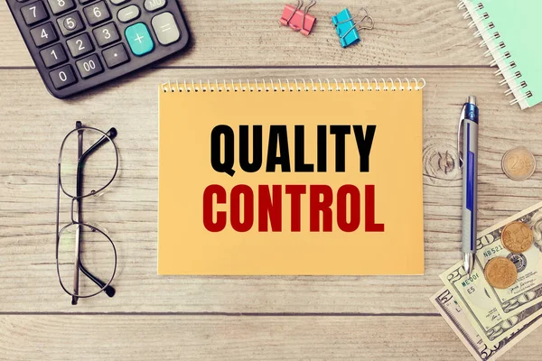 Quality Control is written on a notepad on an office desk with office accessories.