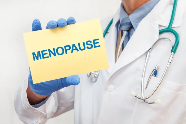 Close-up of a male doctor in gloves holding a sign with the text MENOPAUSE