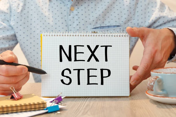 Ofis masasında kırtasiye arasında NEXT STEP metni bulunan defter.