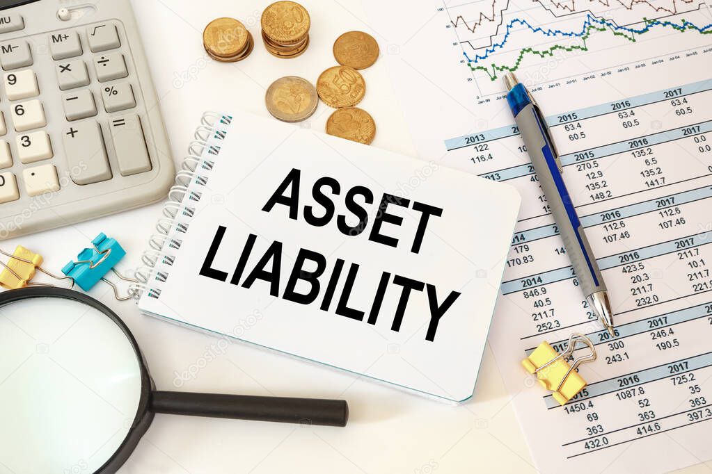 Asset Liability is written on a notepad on an office desk with office accessories.