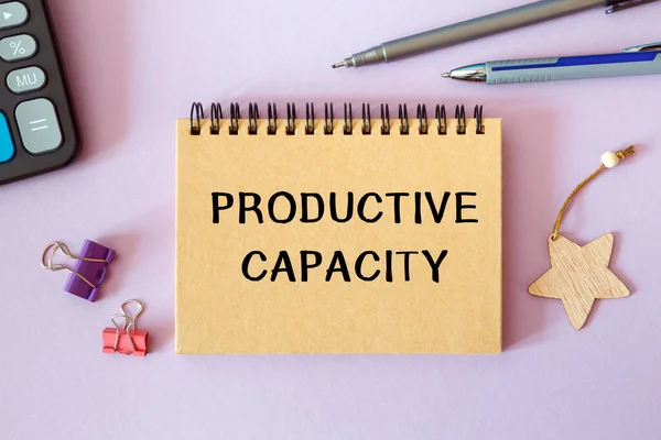 Productive capacity is written on a notepad on an office desk with office accessories.
