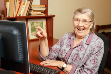 Yaşlı bir kadın bilgisayar okuyor ve interneti izliyor.