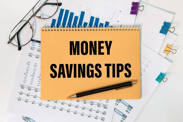 MONEY SAVINGS TIPS is written on a notepad on an office desk with office accessories.