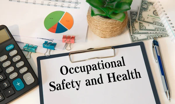 Paper with Occupational Safety and Health on the office table, calculator and office accessories.
