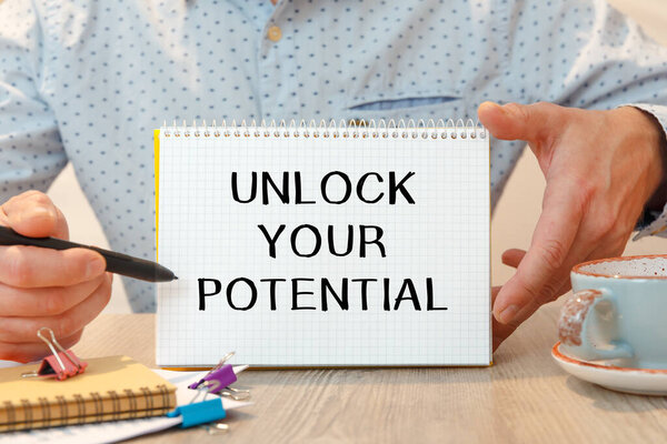 Ноутбук с текстом - Разблокировать свой потенциал - на офисном столе среди канцелярских товаров.