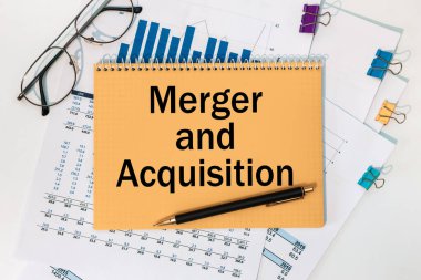 Ofis masasında kırtasiye arasında birleşme ve satın alma metni bulunan defter.