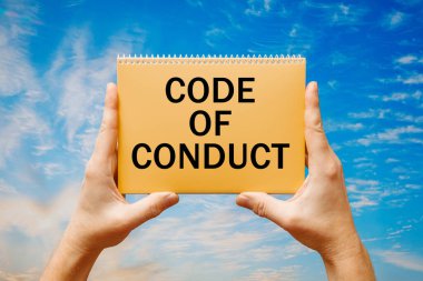 Mavi bir gökyüzünün arka planında üzerinde CONDUCT 'un metin kodları olan bir kart tutan adam.