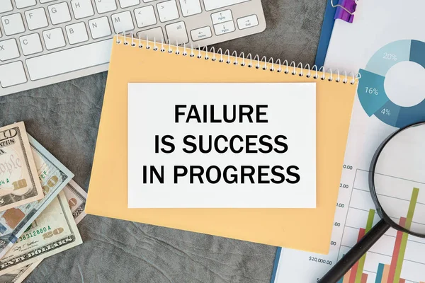 Failure Is Success In Progress is written in a document on the office desk with office accessories, money and diagram