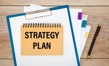 Üzerinde STRATEGY PLAN yazan not defteri, dokümanlar ve tahta bir masa üzerinde bir kalem