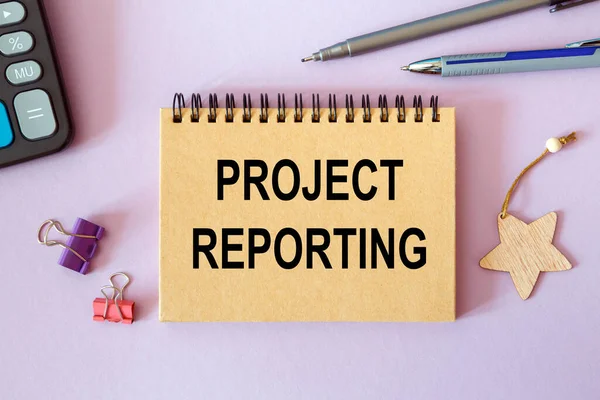 Project Reporting - written on a notepad on an office desk with office accessories.