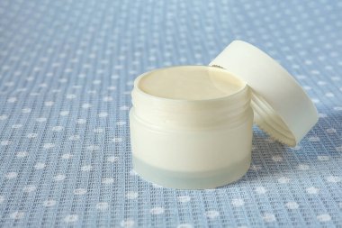 Gri-mavi arka planda kozmetik kremi olan beyaz kavanoz..