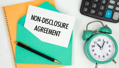 Bir posta zarfındaki kart İfşa Olmama Anlaşması, saat, hesap makinesi, kalem.