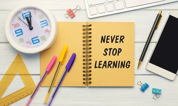 Never Stop Learning - an inscription on a notebook on a table with a clock and office supplies. Business concept