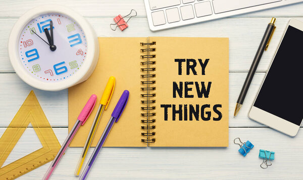 TRY NEW THINGS - an inscription on a notebook on a table with a clock and office supplies. Business concept