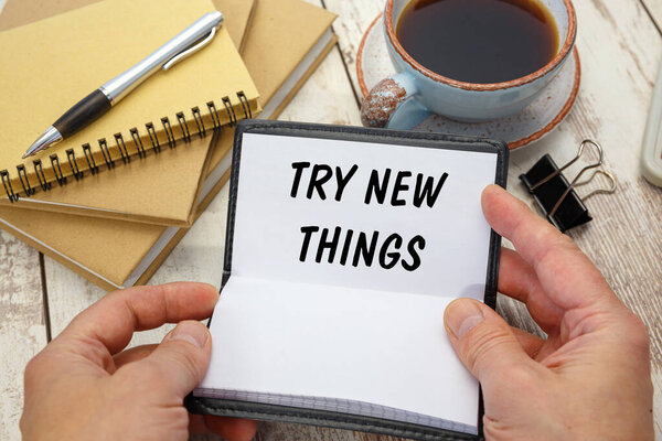 Hands open a notebook with the inscription TRY NEW THINGSon the background of the office desk