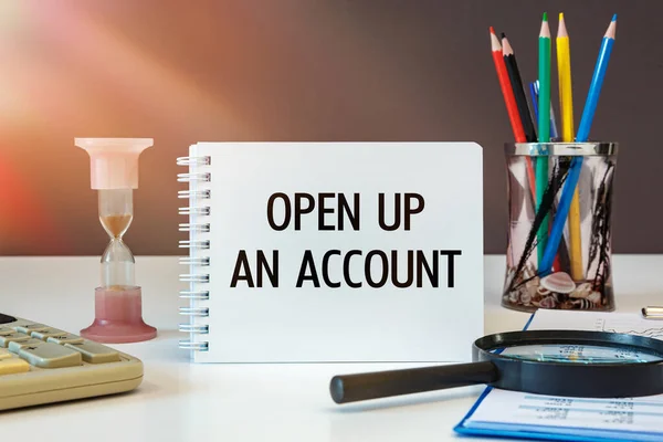 OPEN UP AN ACCOUNT is written on a notepad on an office desk with office accessories.