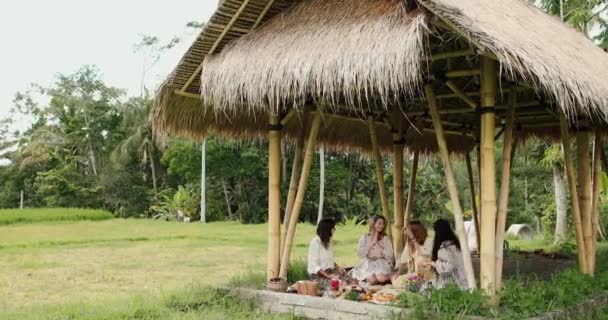 Чотири жінки сидять на землі зі складеними ногами під час пікніка і розмовляють — стокове відео