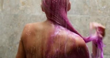 Sırtında bileziklerle çıplak bir kız boyalı pembe saçlarını duşta yıkıyor.
